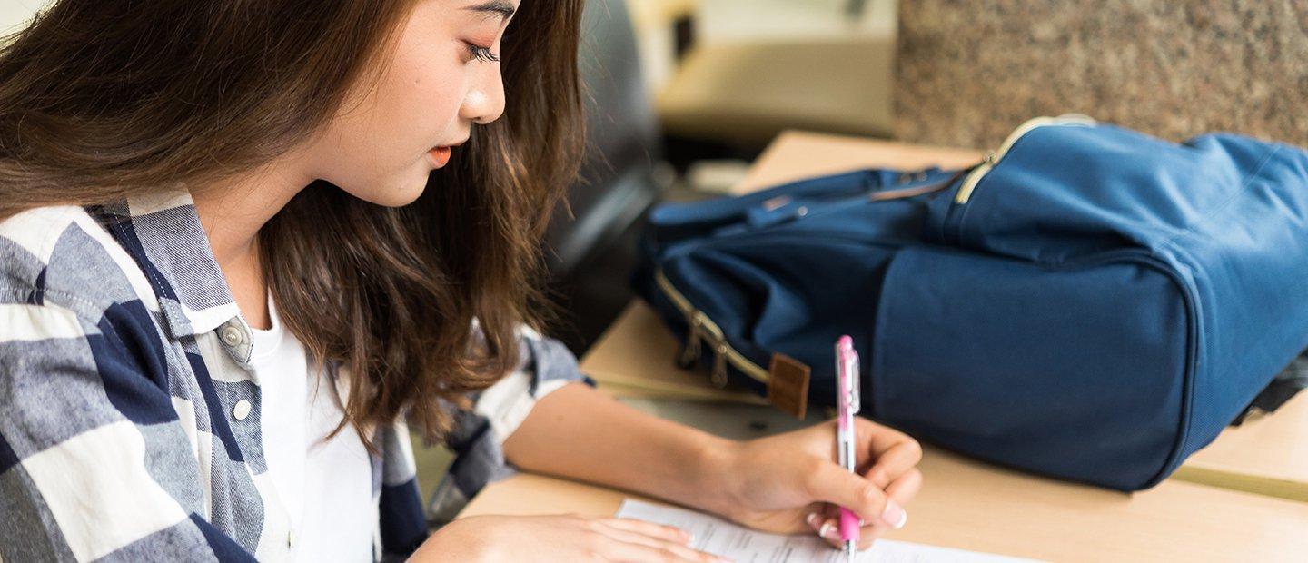 A female student seated at a desk, filling out a form.